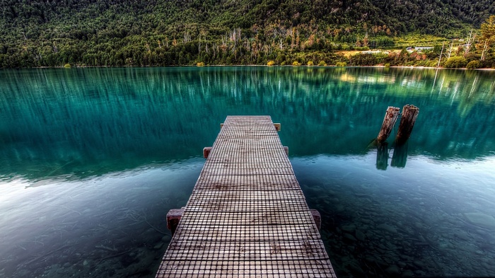 Wooden pier on a calm turquoise lake with a forest background