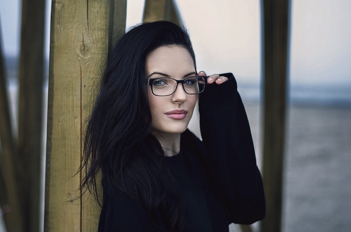 Woman with black hair and glasses by wooden post