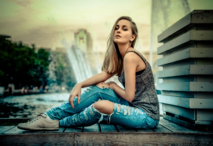 Woman in torn jeans sitting by a fountain