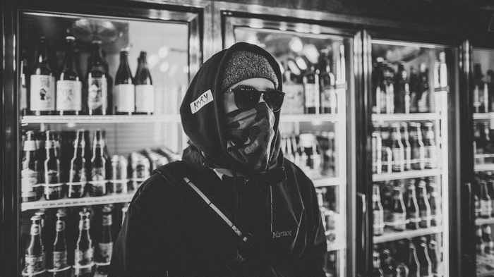 Person in sunglasses and mask in front of beer refrigerators