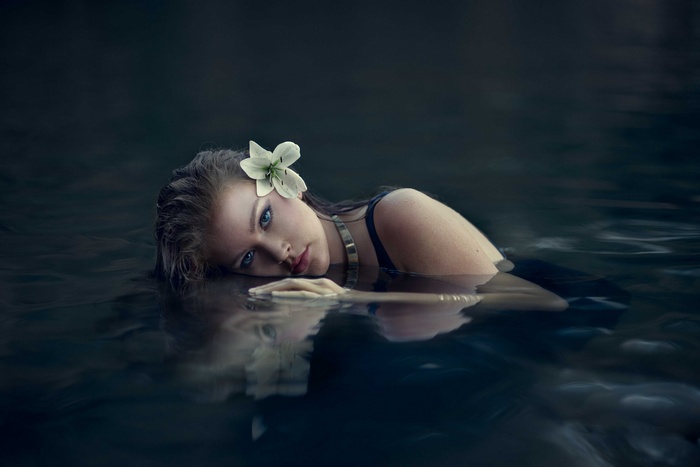 Woman with flower in wet hair in dark water