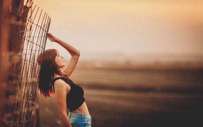Woman in black top and jeans leaning on fence
