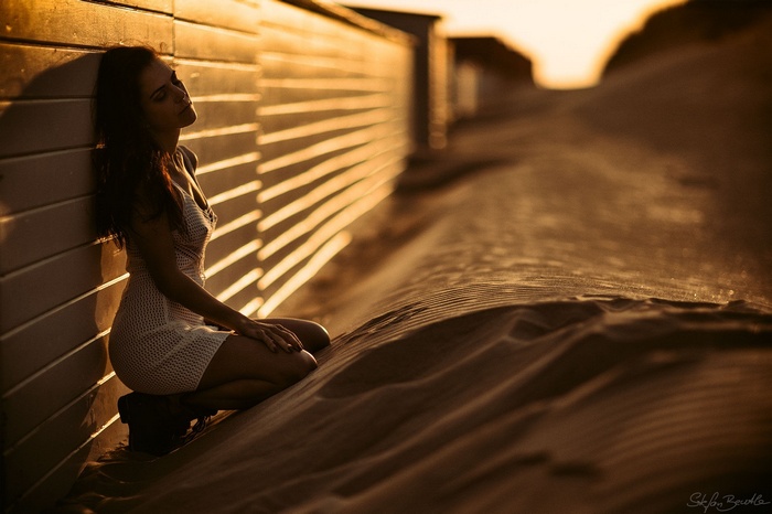 Woman in white dress on sand at sunset
