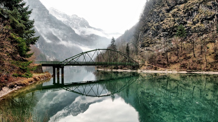 Green bridge over a lake with misty mountains