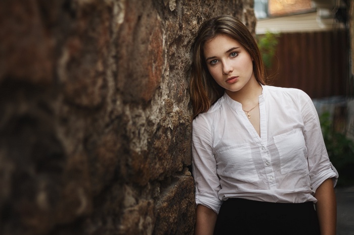 Young woman in white shirt leaning against a stone wall