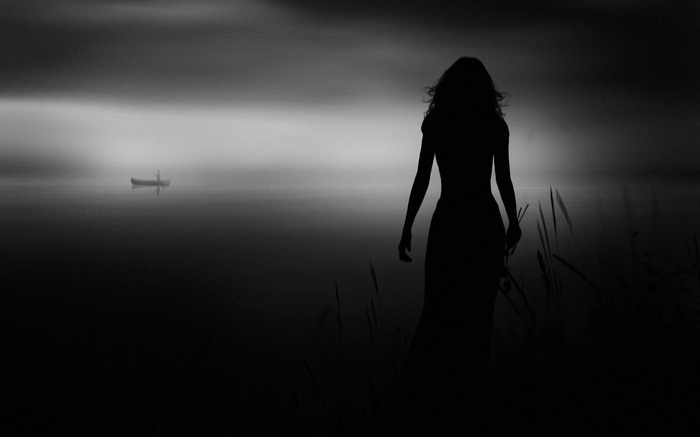 Woman in silhouette by a misty lake with a boat