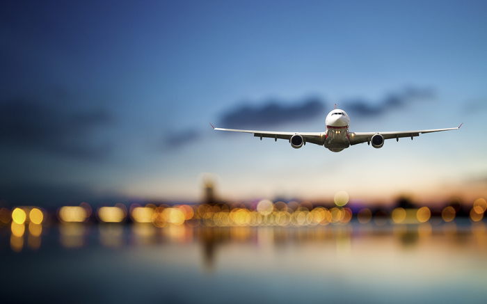 Airplane flying over city lights at dusk