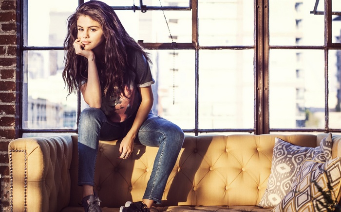 Selena Gomez sitting on a couch in front of a window