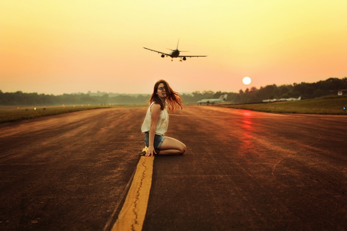 Woman kneeling on runway with airplane landing at sunset