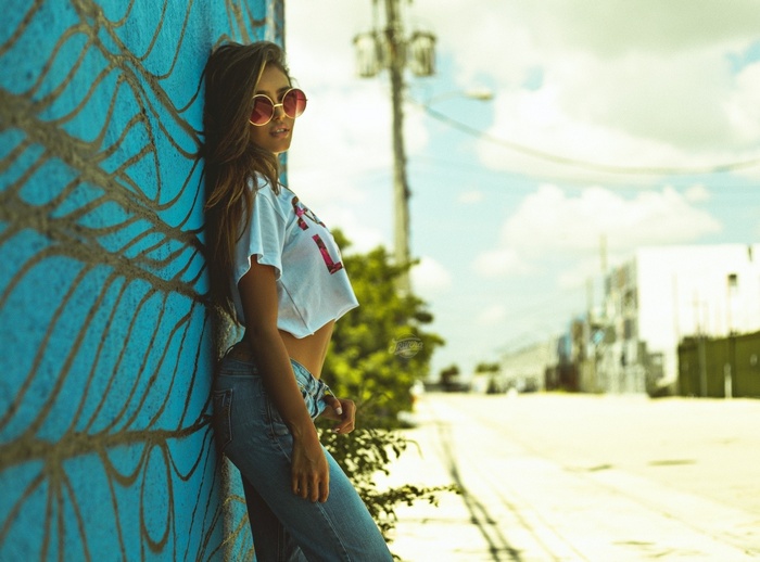 Woman in jeans and crop top leaning against a graffiti wall