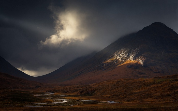 Sunbeams illuminate mountains and a river in a dark landscape