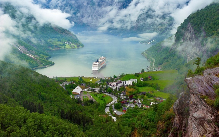 Cruise ship in Geiranger Fjord, Norway, surrounded by mountains and clouds