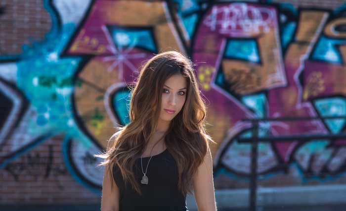 Woman in black tank top in front of graffiti wall
