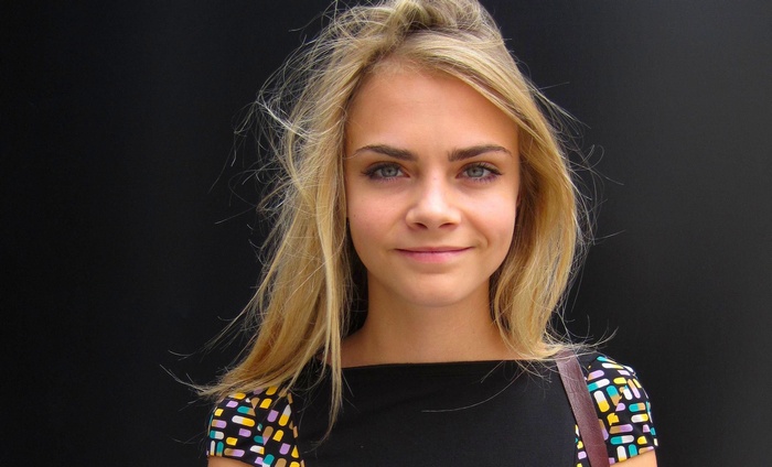 Cara Delevingne posing in front of a black background