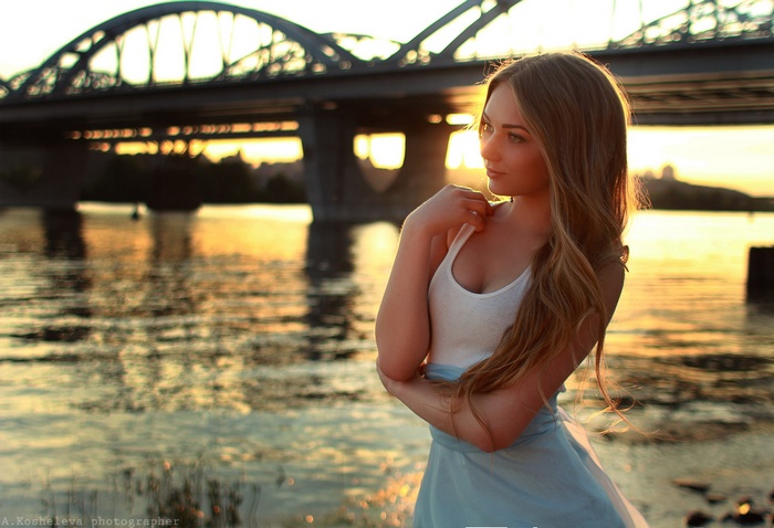 Woman by the river at sunset under a bridge