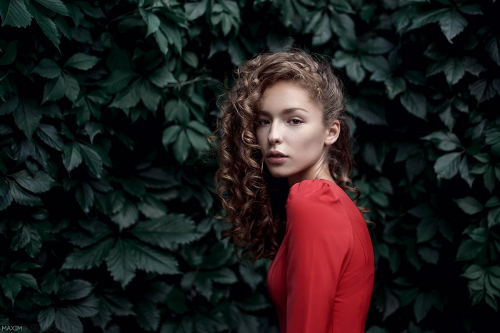 Woman with curly hair in red dress near leaves