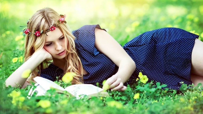 Woman with flower crown reading a book in a field