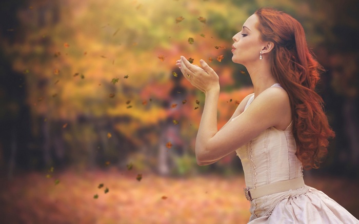 Woman in white dress blowing leaves in autumn