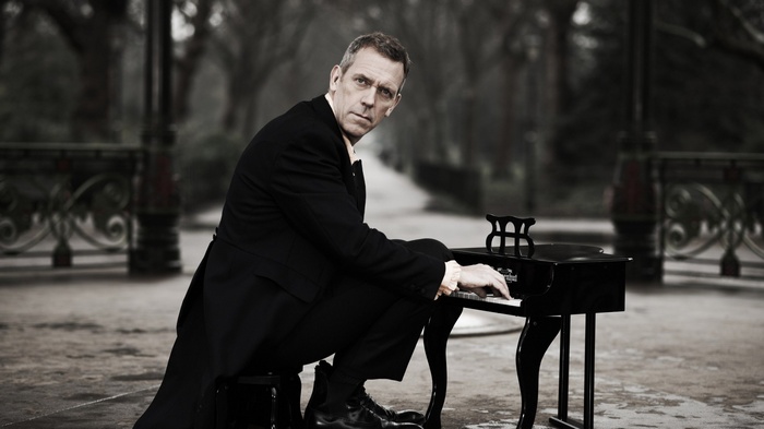 Hugh Laurie plays a miniature piano in a park