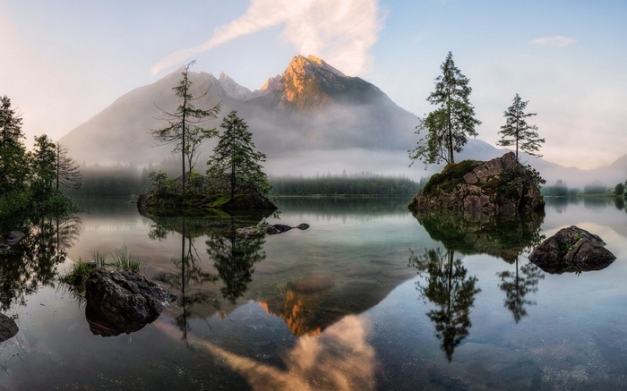 Misty mountains reflected in a calm lake with trees
