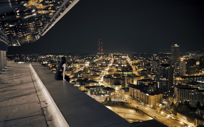 Woman sitting on a rooftop overlooking a city at night