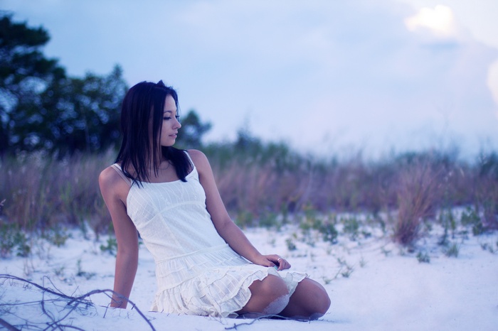 Woman in white dress sitting on sand