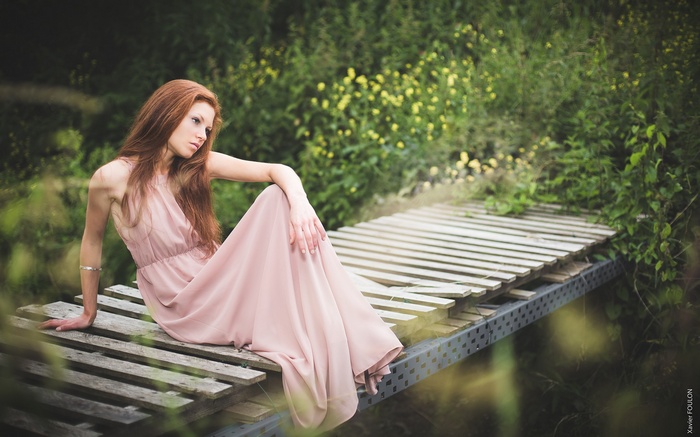 Redhead woman in pink dress sitting on a wooden bridge