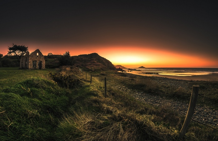 Ruined building on a grassy coast at sunset