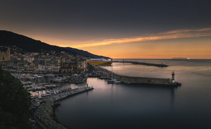 Coastal town harbor with ferry and lighthouse at sunset