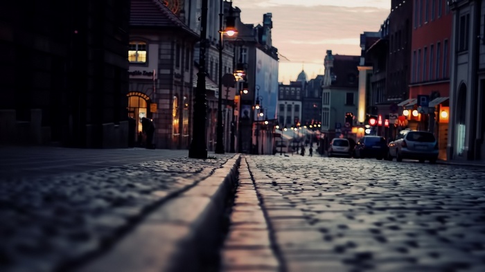 Cobblestone street with cars and buildings at dusk