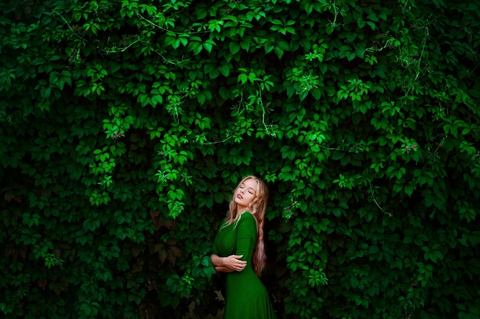 Ann Nevreva in a green dress against a wall of leaves