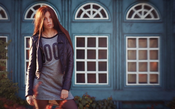 Woman in jacket and dress standing in front of blue building