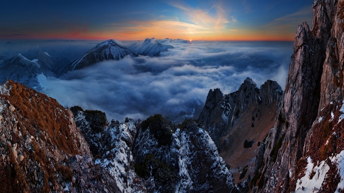 Sunset over snowy mountains above clouds and cliffs
