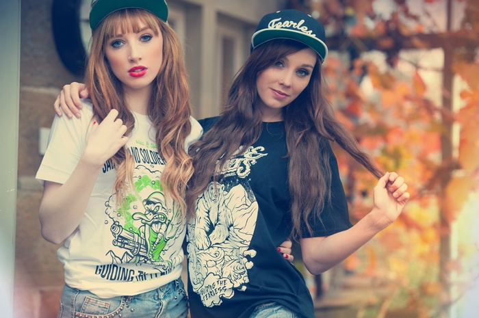Two young women wearing baseball caps and graphic t-shirts
