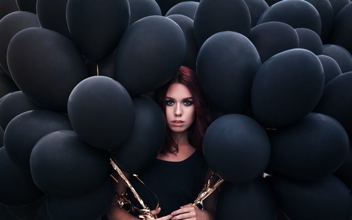 Woman with red hair surrounded by black balloons
