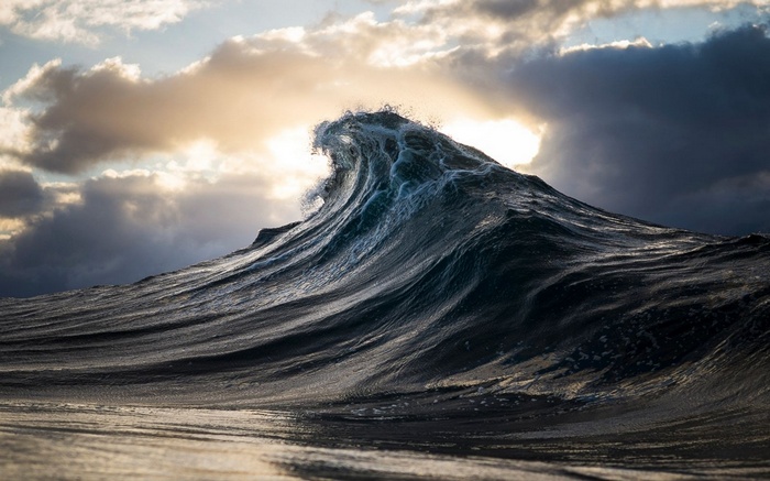 A large wave crashes under dramatic clouds