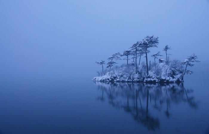 Snowy island with trees and cabins in a misty lake in Japan