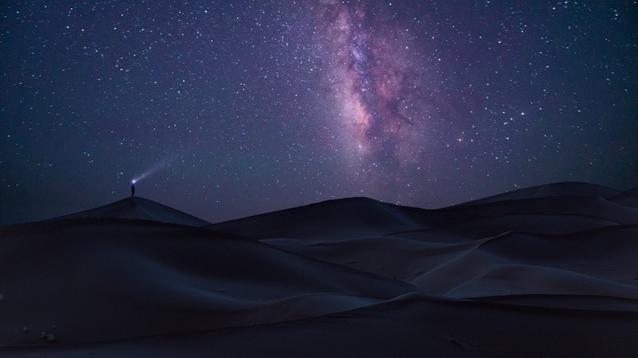 Person with flashlight under the Milky Way in the desert