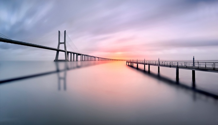 Vasco da Gama Bridge and pier at sunset over calm water