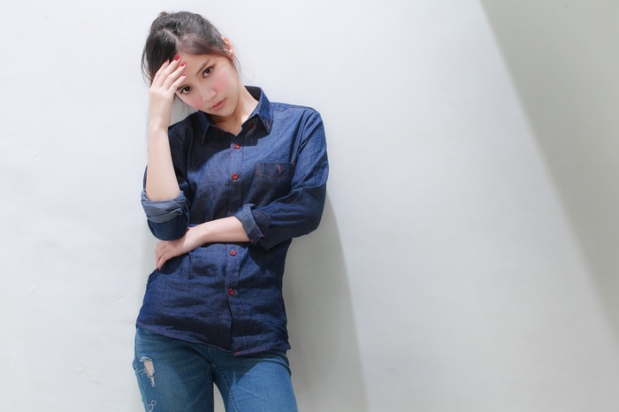 Asian woman in denim shirt and jeans leaning against wall