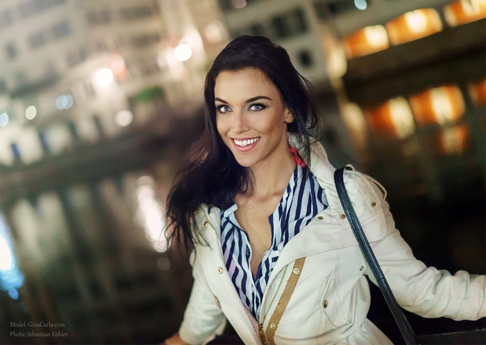 Gina Carla smiles in a white jacket at night