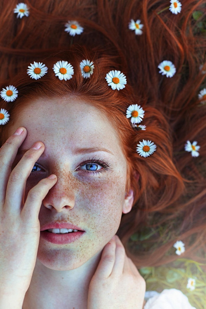Redhead woman with freckles and blue eyes adorned with daisies