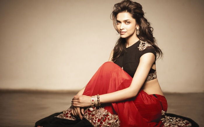 Deepika Padukone sitting in a red and black outfit