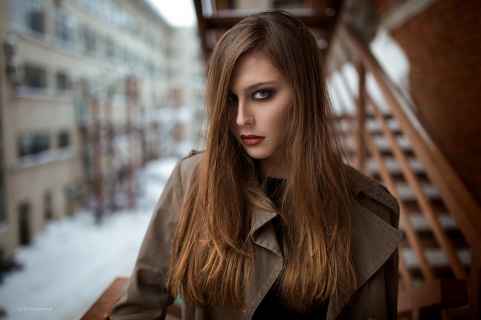 Woman with long brown hair and smoky eyes wearing a trench coat