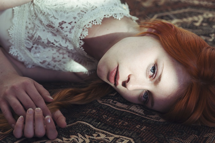 Redhead woman with blue eyes lying on a rug