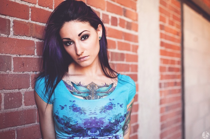 Woman with tattoos leaning against a brick wall