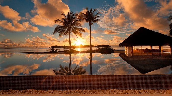 Tropical sunset over ocean with infinity pool and hut