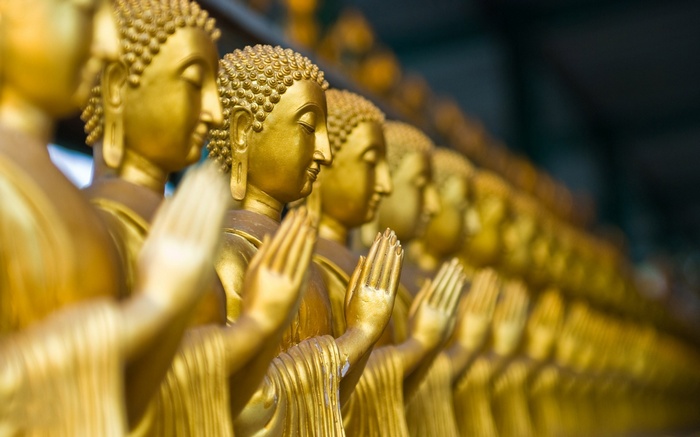 Row of golden Buddha statues with praying hands