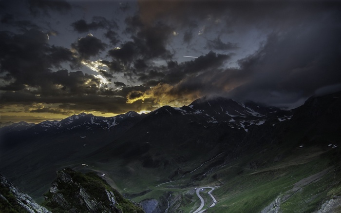 Dark mountain valley with winding road at sunset