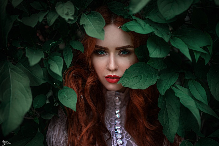 Redhead woman with green eyes behind leaves